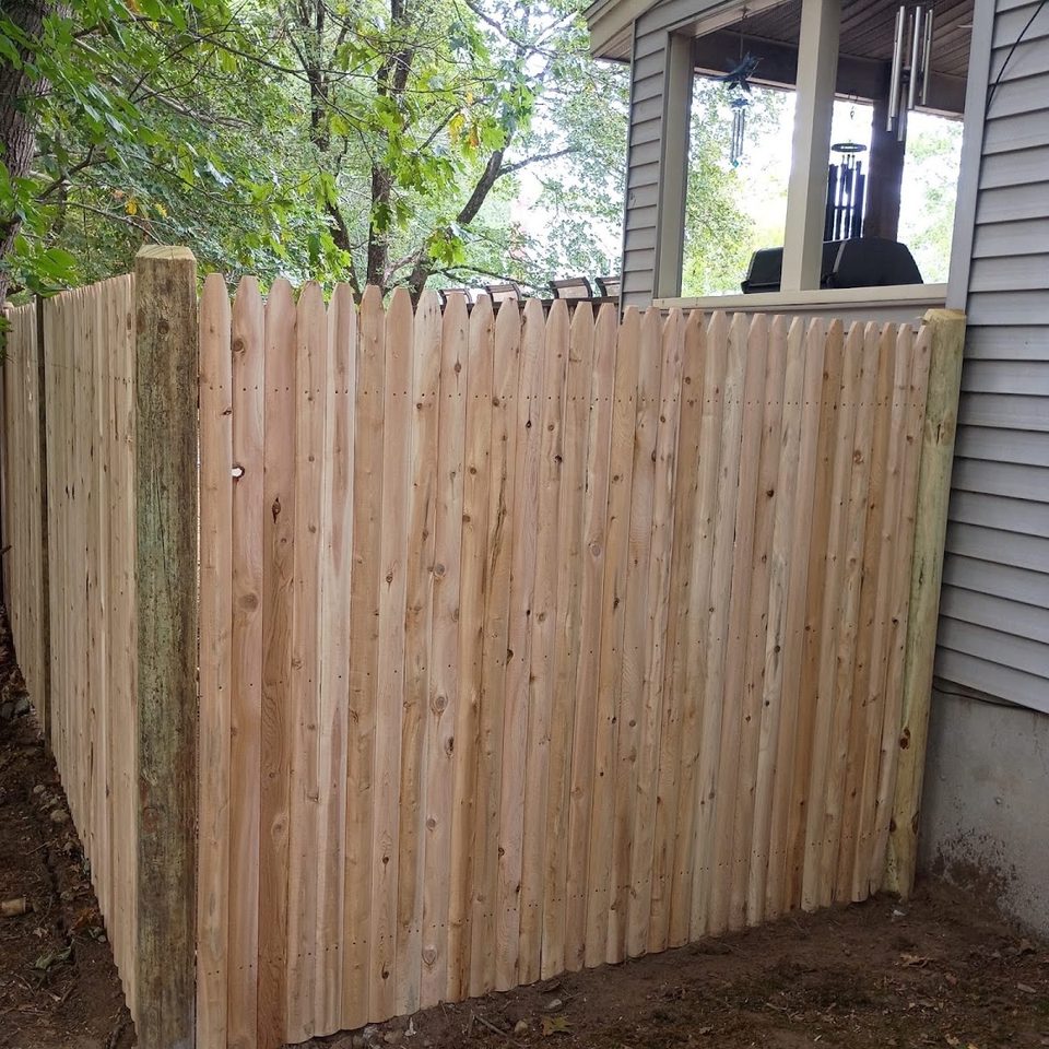 Tall cedar privacy fence installed tight against a house wall