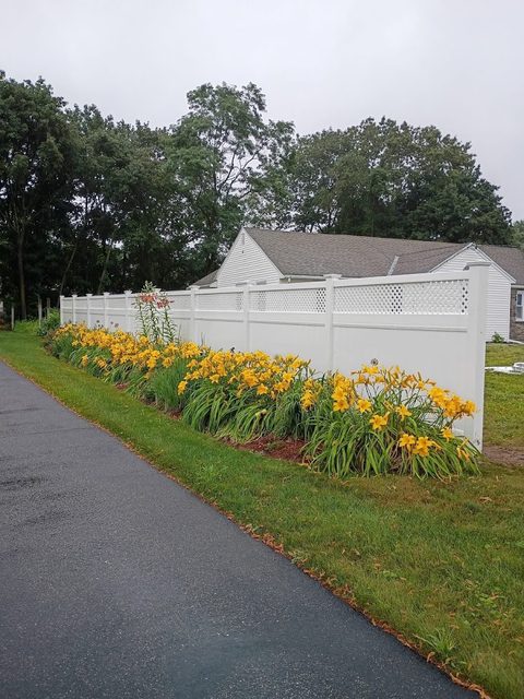 Vinyl fence alongside a spring flower bed and driveway