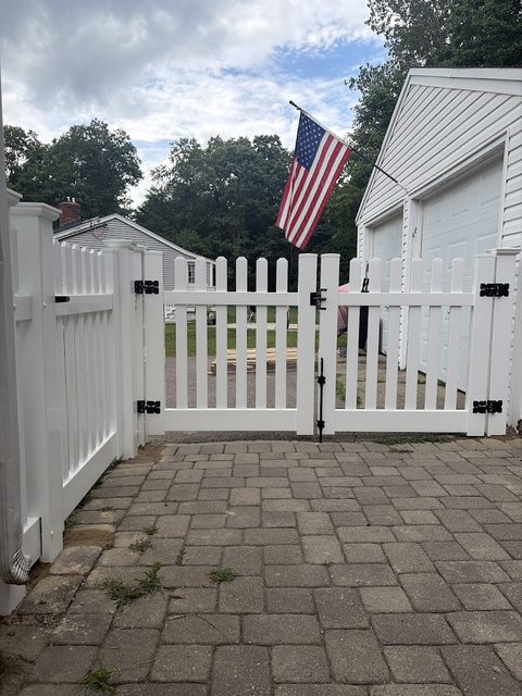 White vinyl picket gate framing a paved front entrance