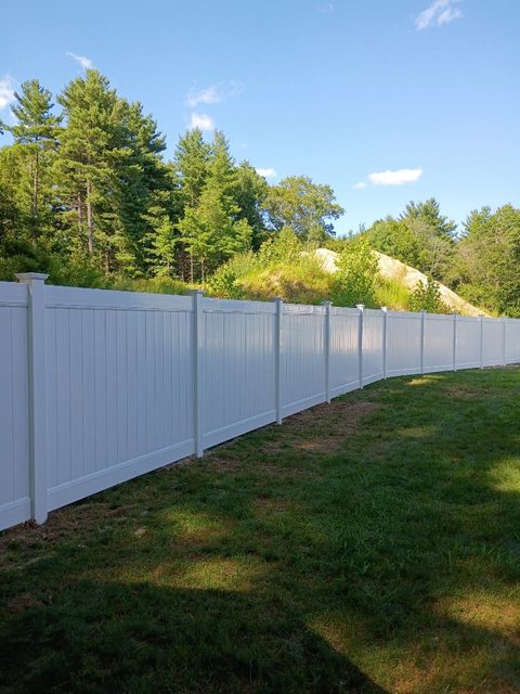 White vinyl privacy fence set against a mature tree line